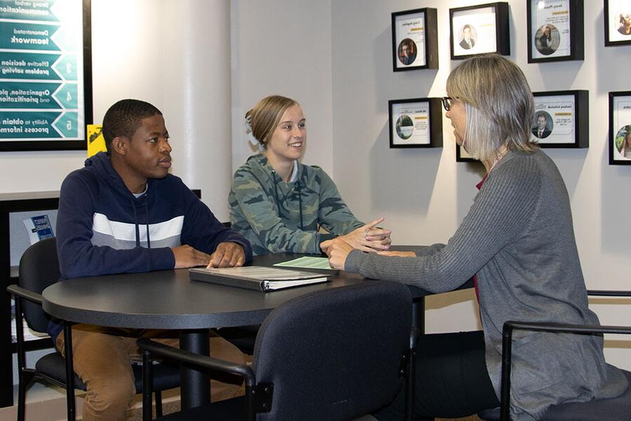 NWU administrator sits with two students at a table in a conference room.